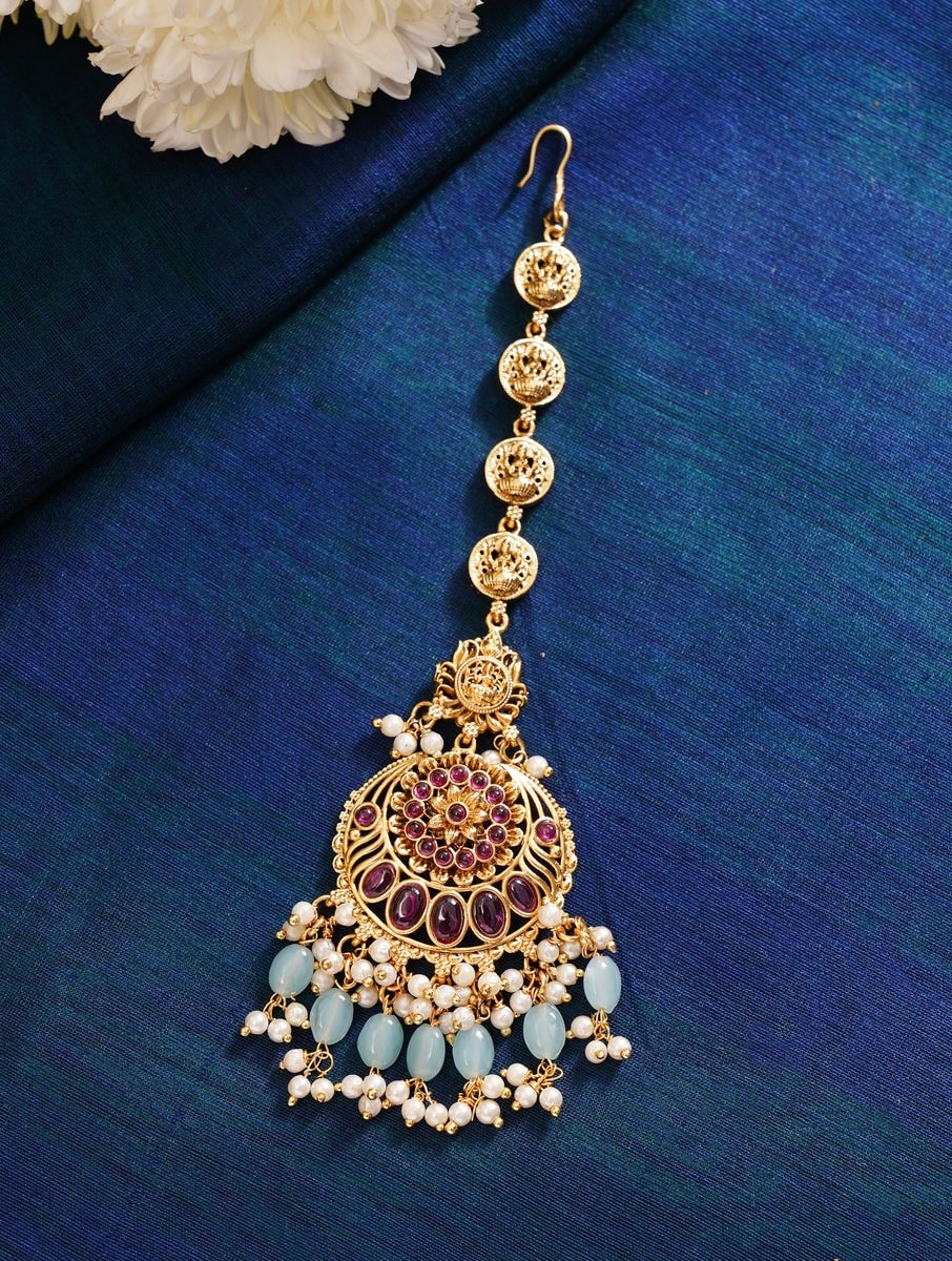 Golden Plated KempStone Studed Maangtikka with intricate design and pearl accents on blue background