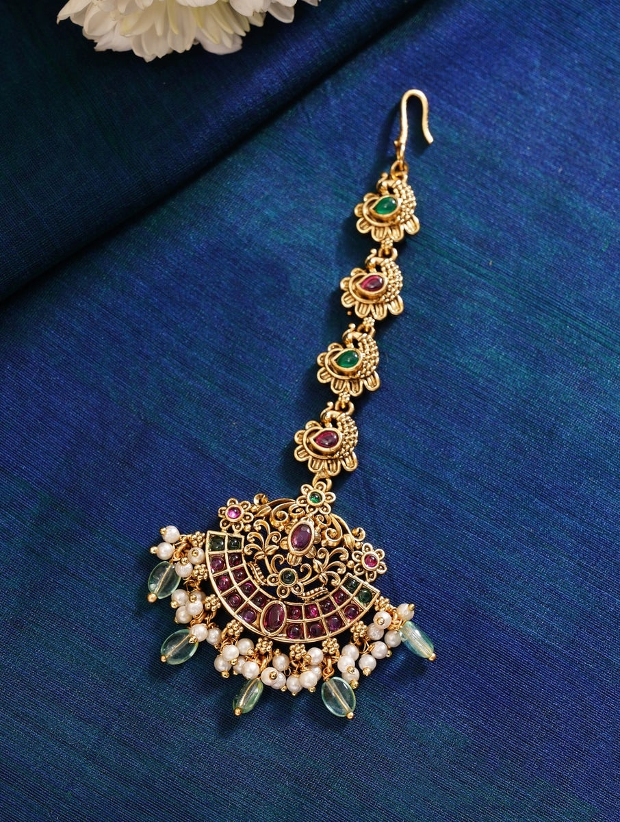 Matt Gold Plated KempStone Studed Maangtikka with intricate floral design and dangling pearls on blue fabric