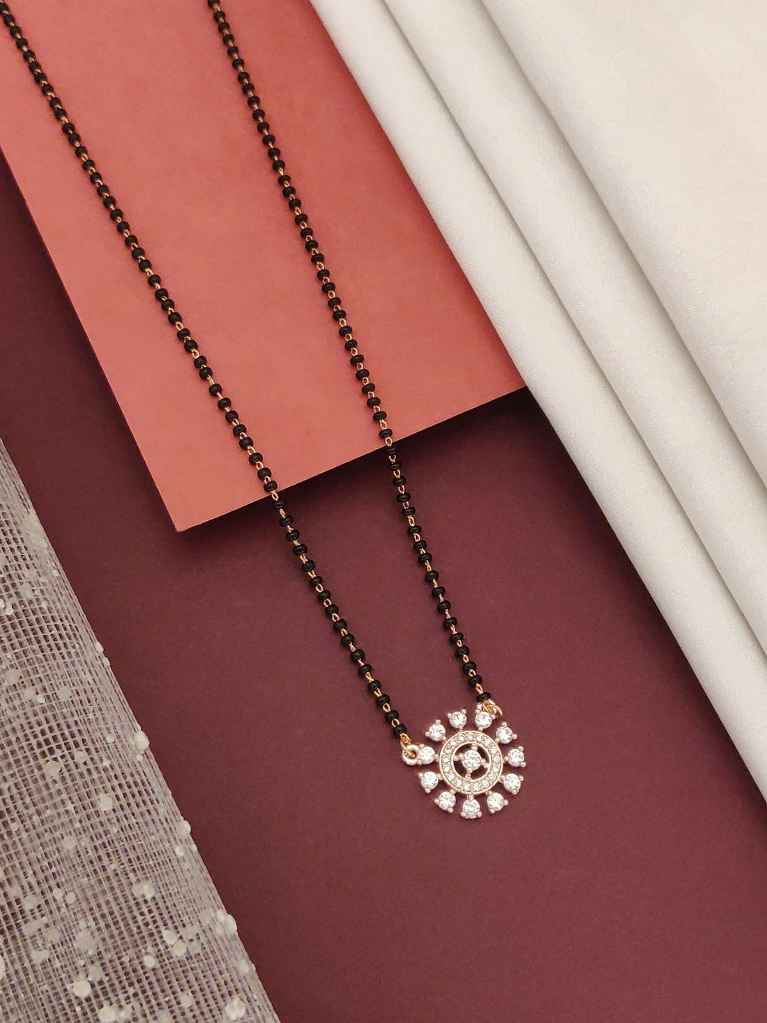 Abdesignsjewellery rose gold plated diamond mangalsutra with black beads and circular diamond pendant on maroon backdrop