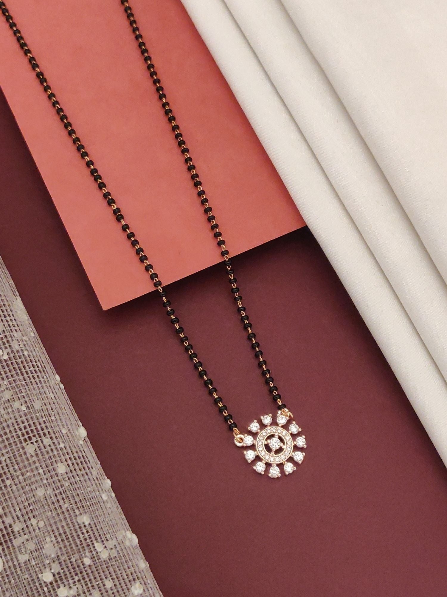Abdesignsjewellery rose gold plated diamond mangalsutra with black beads and circular diamond pendant on maroon backdrop