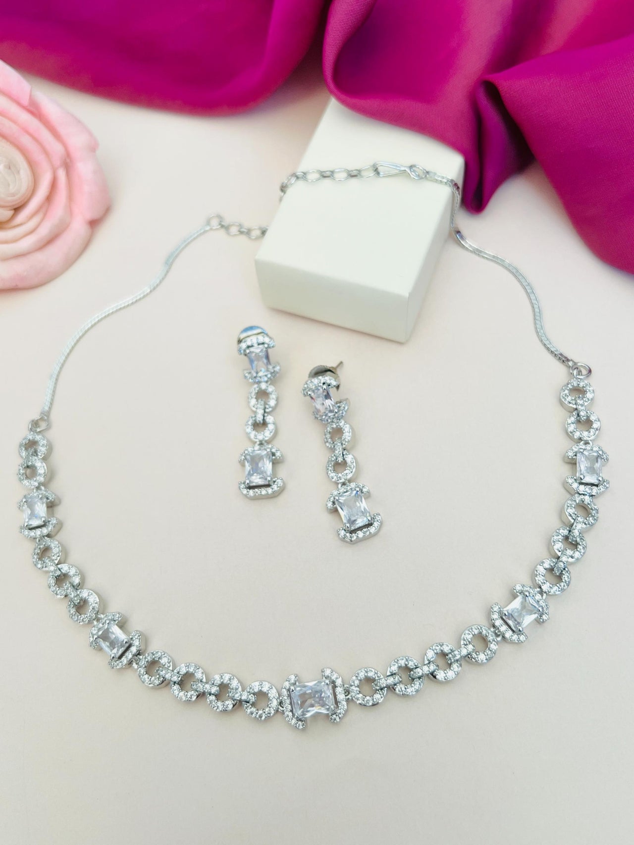 Silver Plated American Diamond Necklace with matching earrings displayed on a white surface with pink fabric background