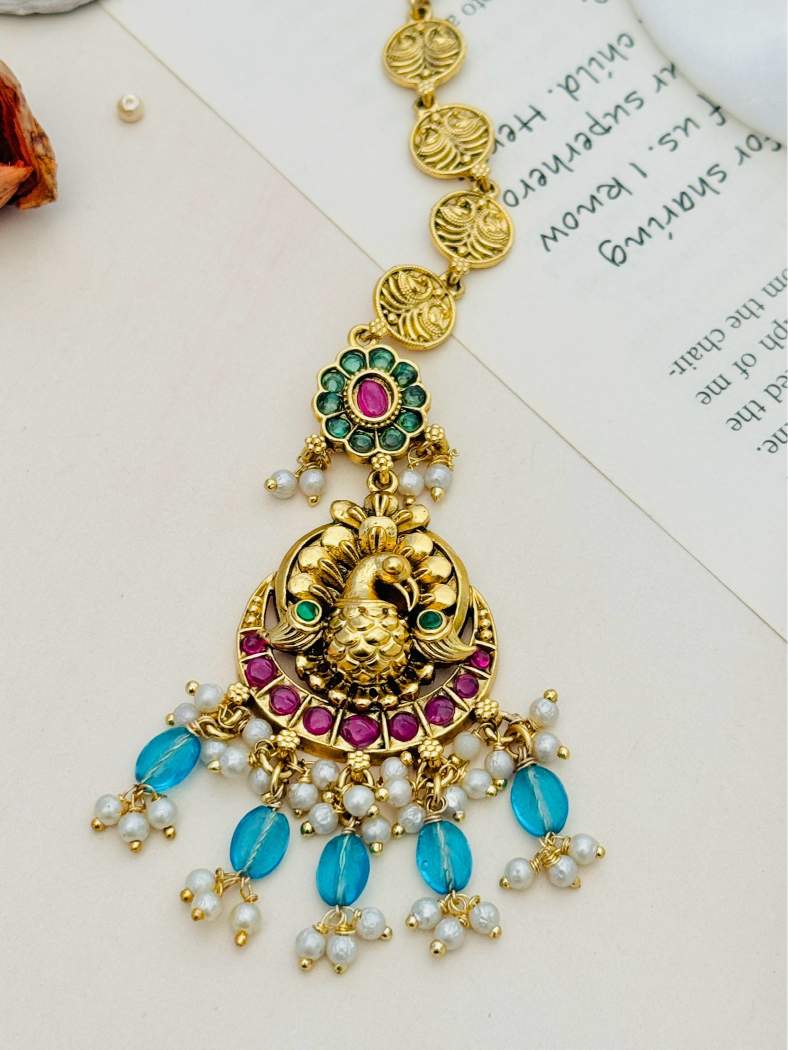 Multistone Sky Blue Matt Gold Plated Peacock Style Maangtikka with intricate gold detailing and pearl accents from Abdesignsjewellery