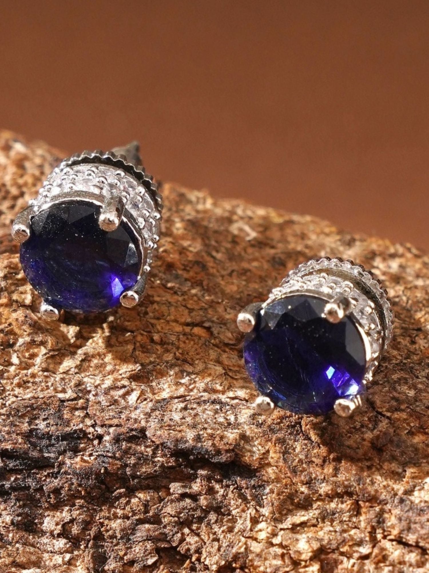 Abdesignsjewellery Precious Silver Plated American Diamond Stud Earring with deep blue stones on textured brown surface