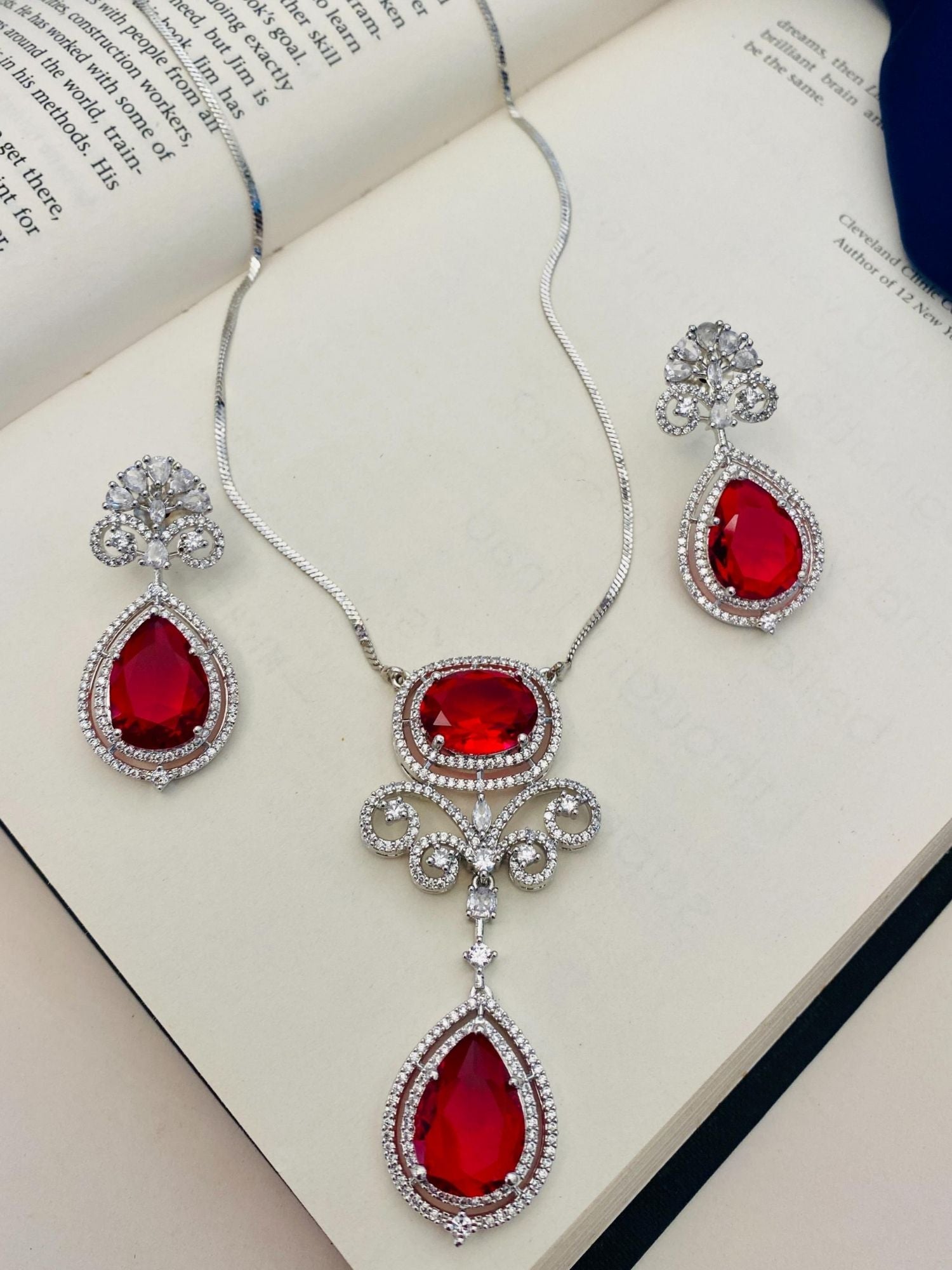silver plated ruby pendant set featuring teardrop red stones with crystal halo and matching earrings on book
