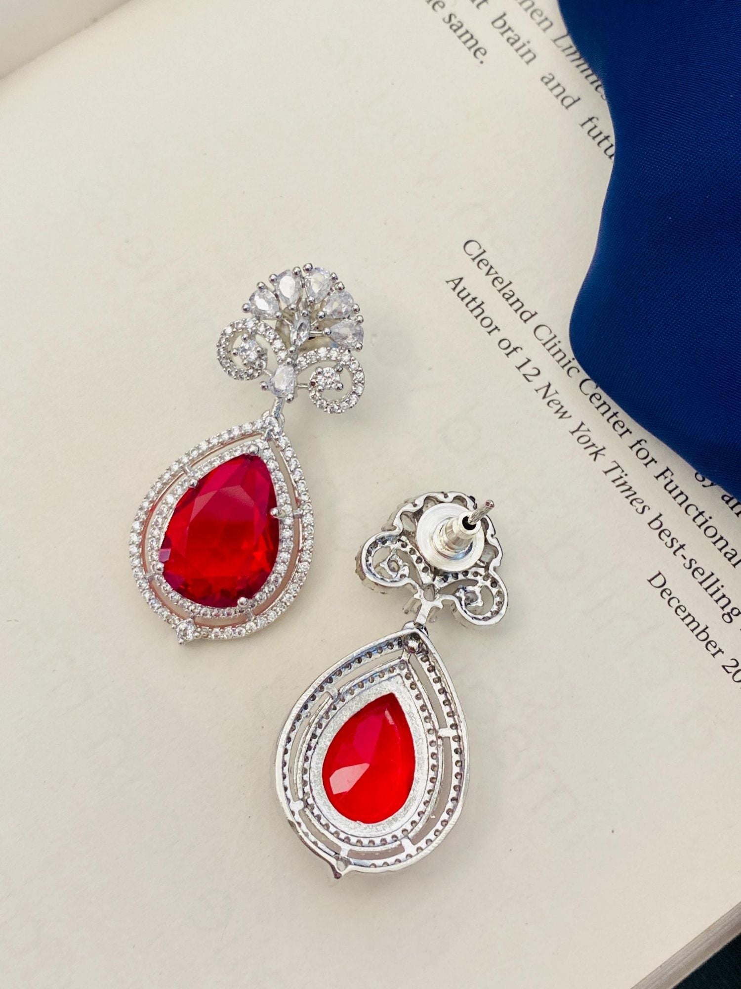 silver plated ruby pendant set teardrop red stones with halo crystals and ornate silver settings on a book