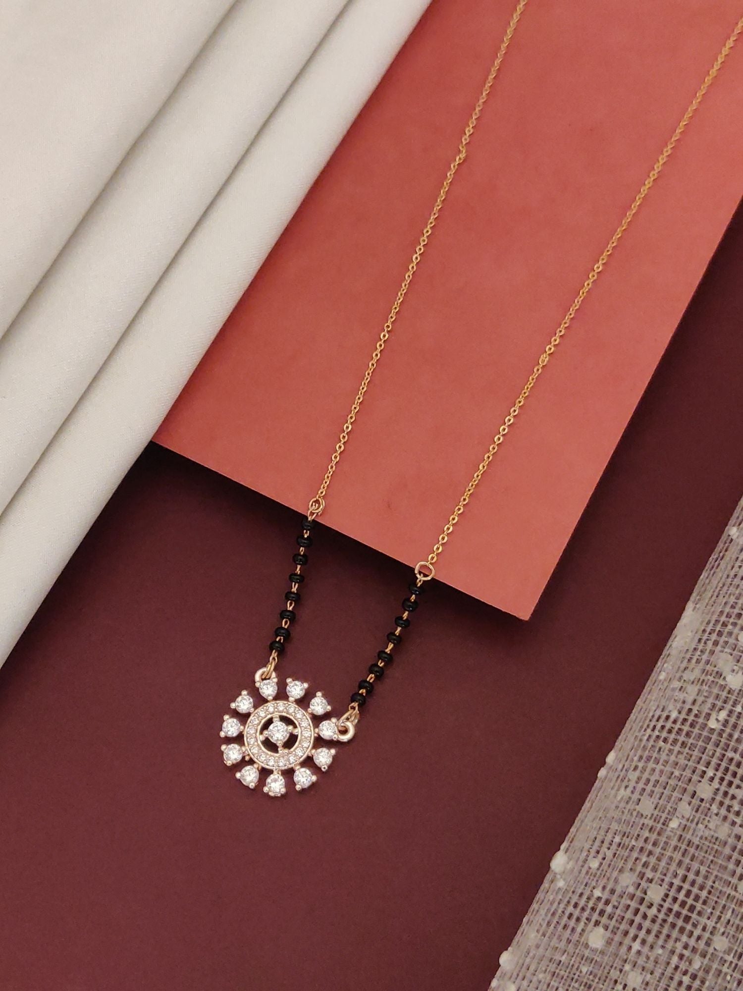 Gold chain mangalsutra with black beads and diamond floral pendant on fabric backdrop buy glamorous mangalsutra jewelry