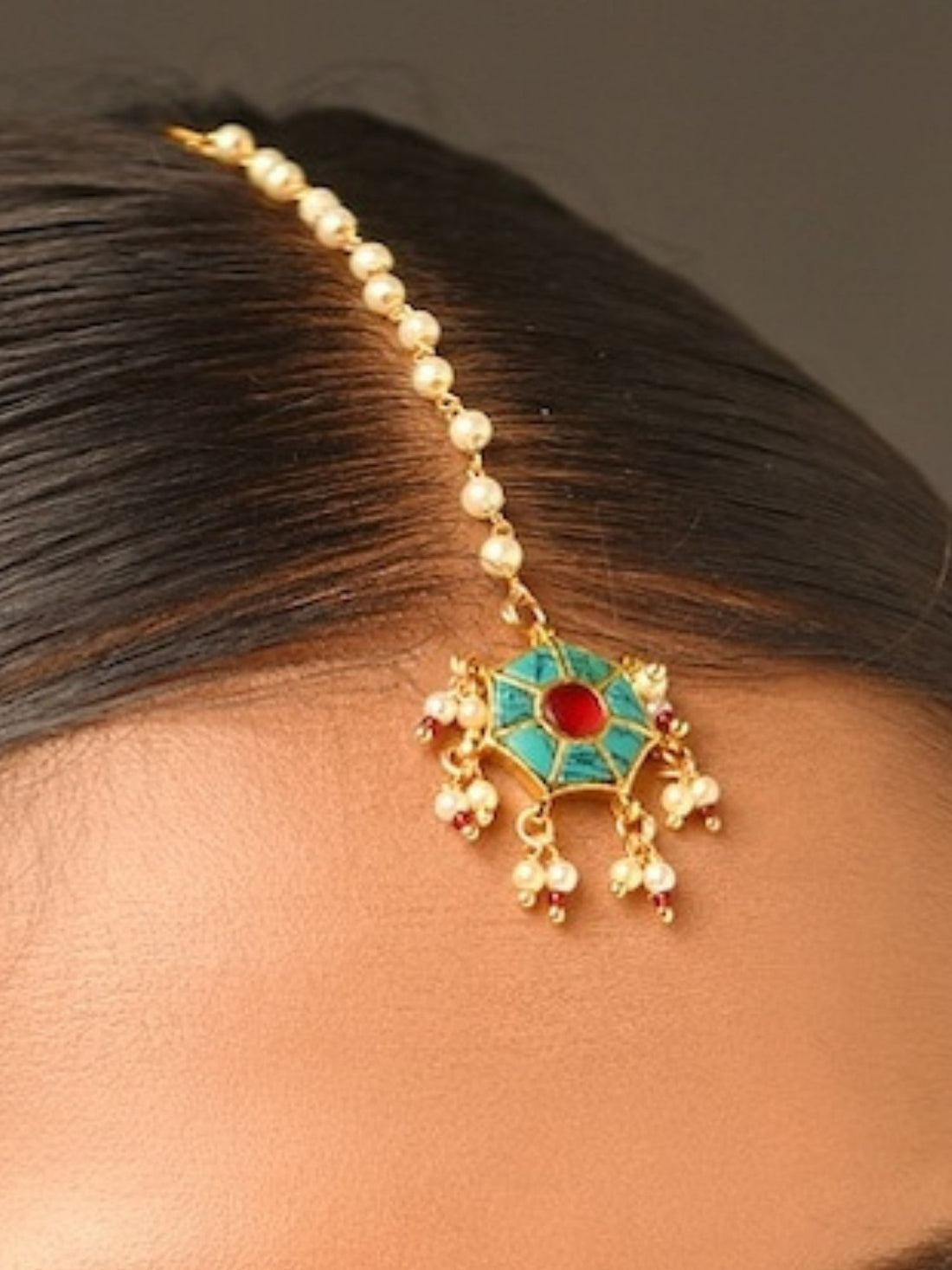 Traditional gold maangtikka with green and red stones worn by woman with sleek hair