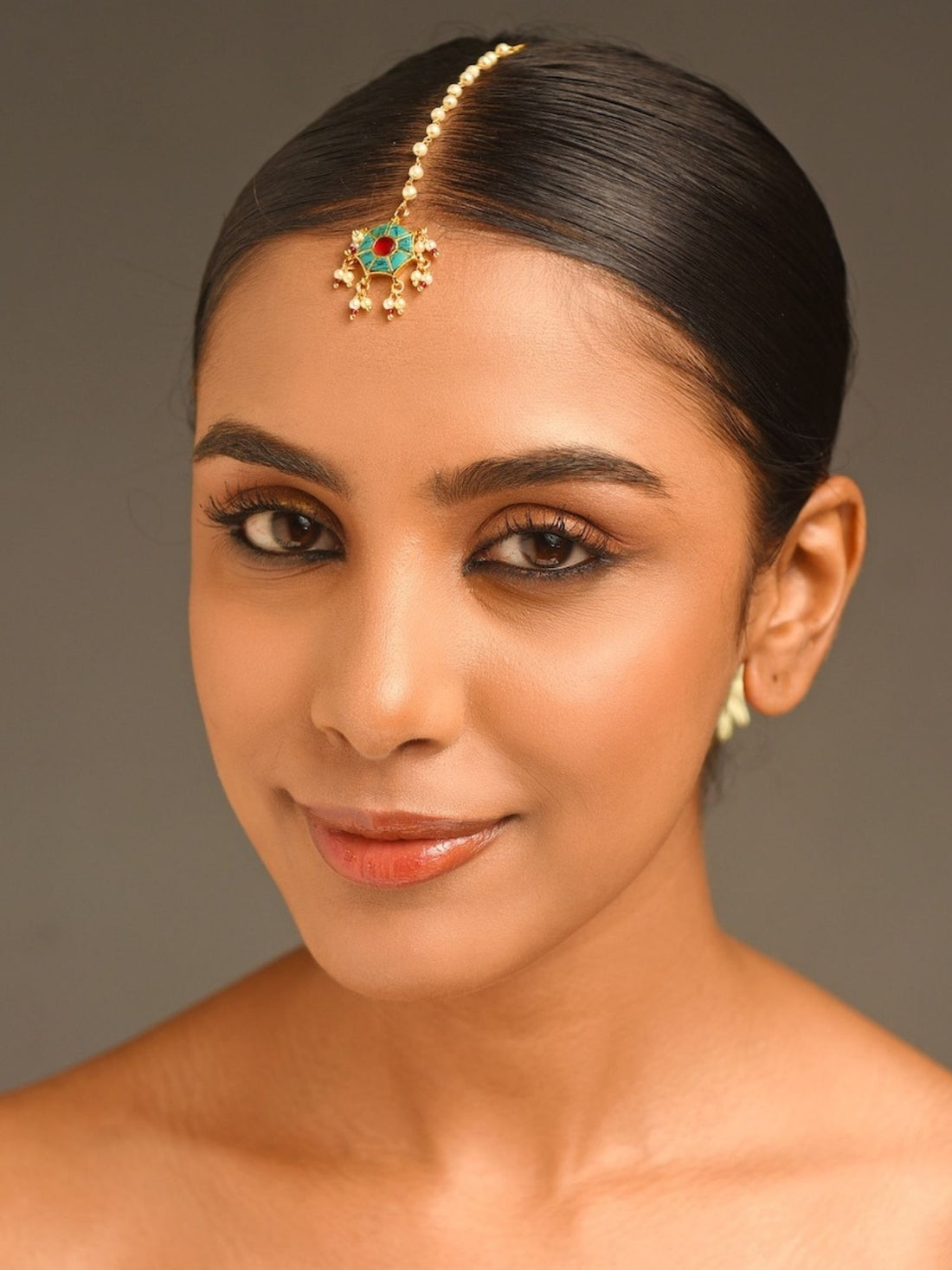 Traditional gold maangtikka with green and red stones worn by woman with sleek hair