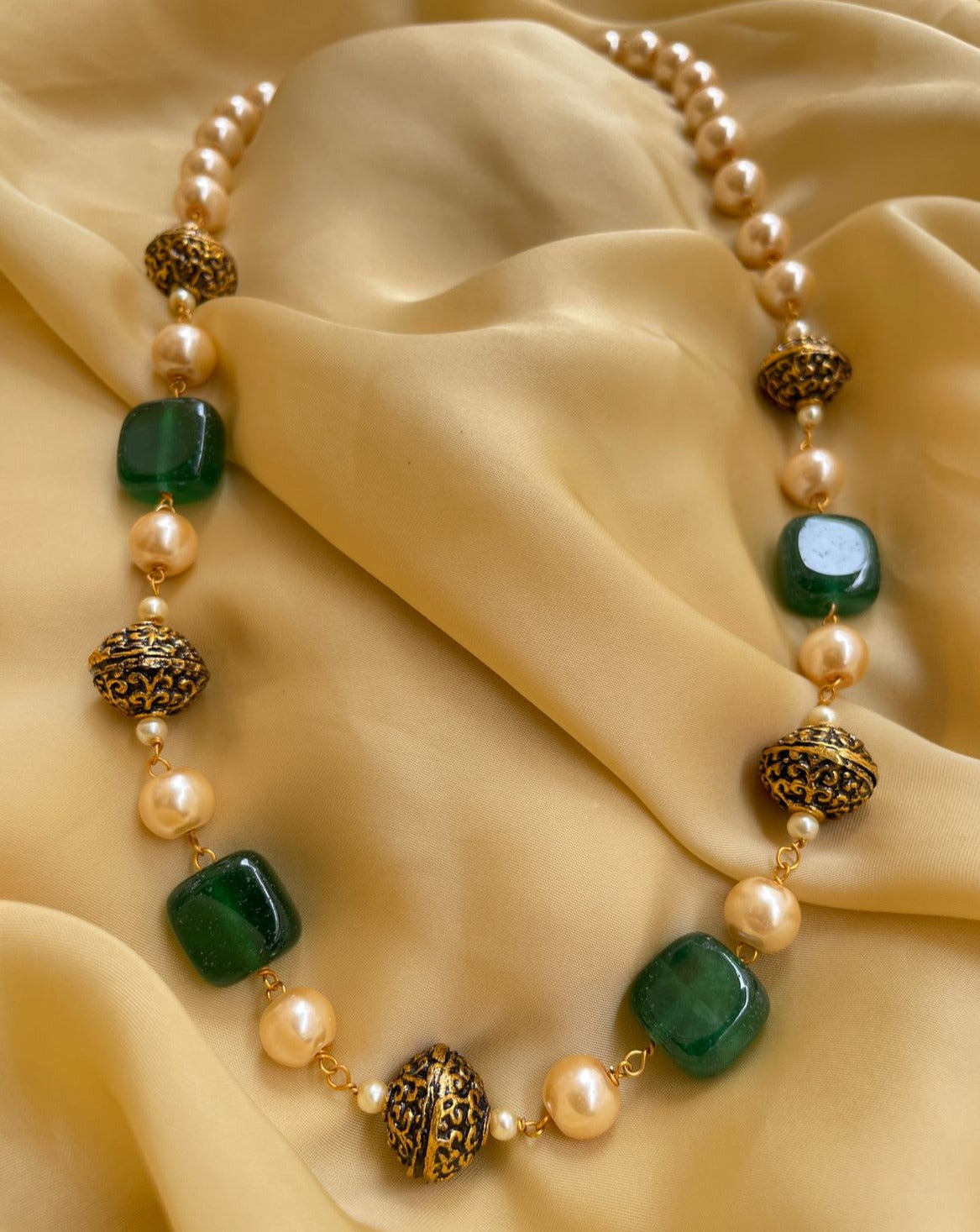 Elegant mala necklace with green gemstones and gold accent beads on soft yellow fabric