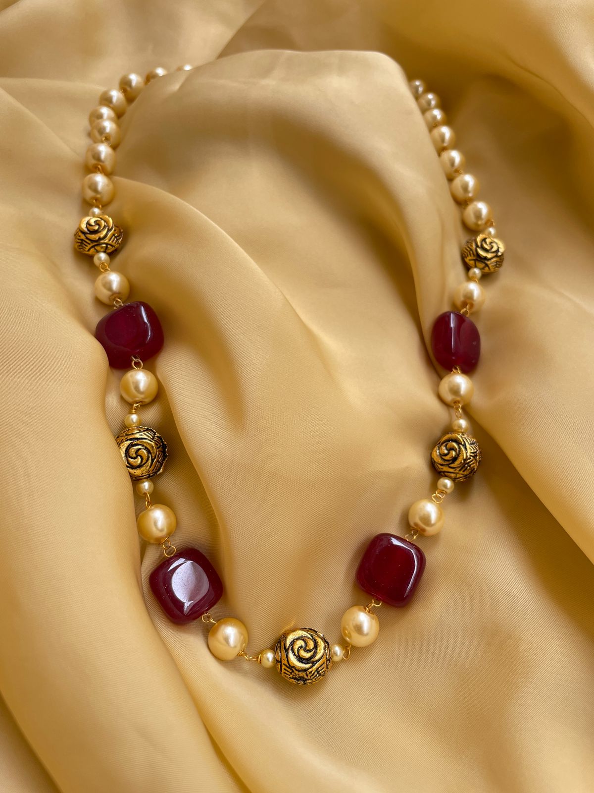 Elegant mala necklace with red stones and golden rose accents on a soft golden fabric background